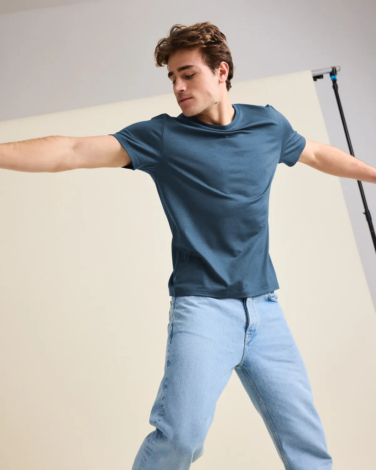 Person wearing a blue merino wool t-shirt and light blue jeans against a neutral background