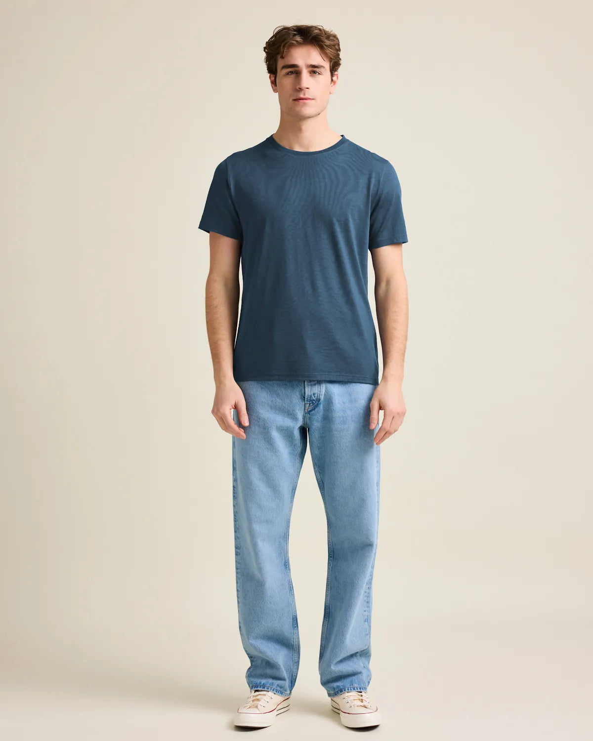 Man wearing a denim-blue merino t-shirt and jeans on a beige background