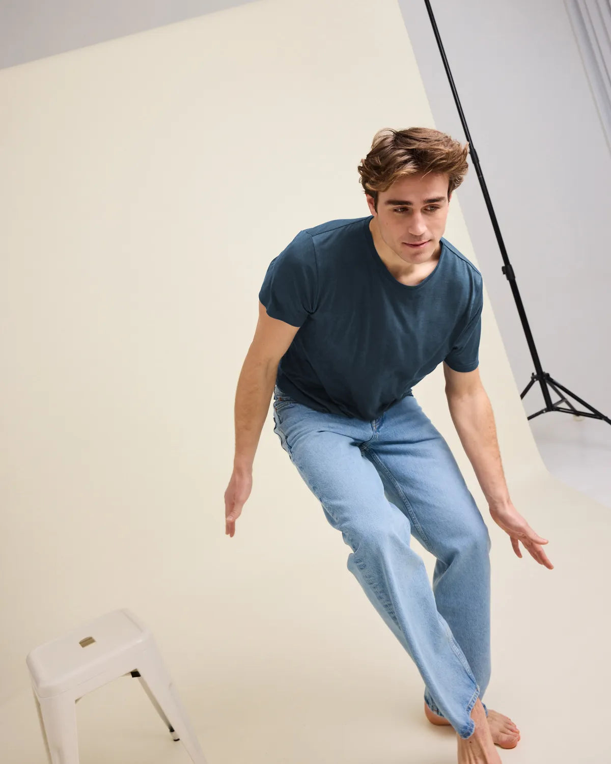 Man wearing a blue merinowool t-shirt and light blue jeans while jumping in a studio