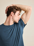 Man wears a short sleeve merino wool T-shirt in denim blue and smells his fresh armpit.