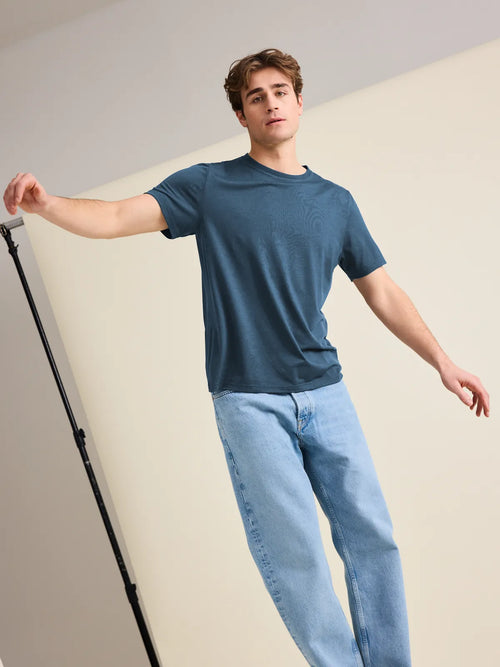 European-crafted, denim blue merino wool T-shirt for men worn by a male model balancing in the studio.