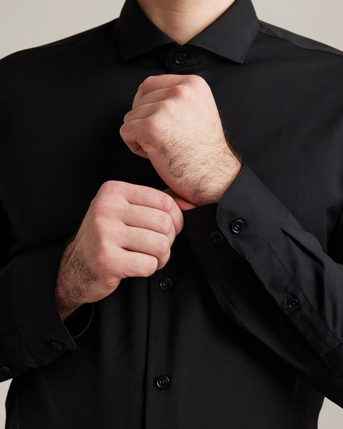 Close up of a man adjusting the cuffs on a black merinowool dress shirt with spread collar