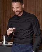 Man in a black merinowool shirt holding a cup of coffee in a cozy setting