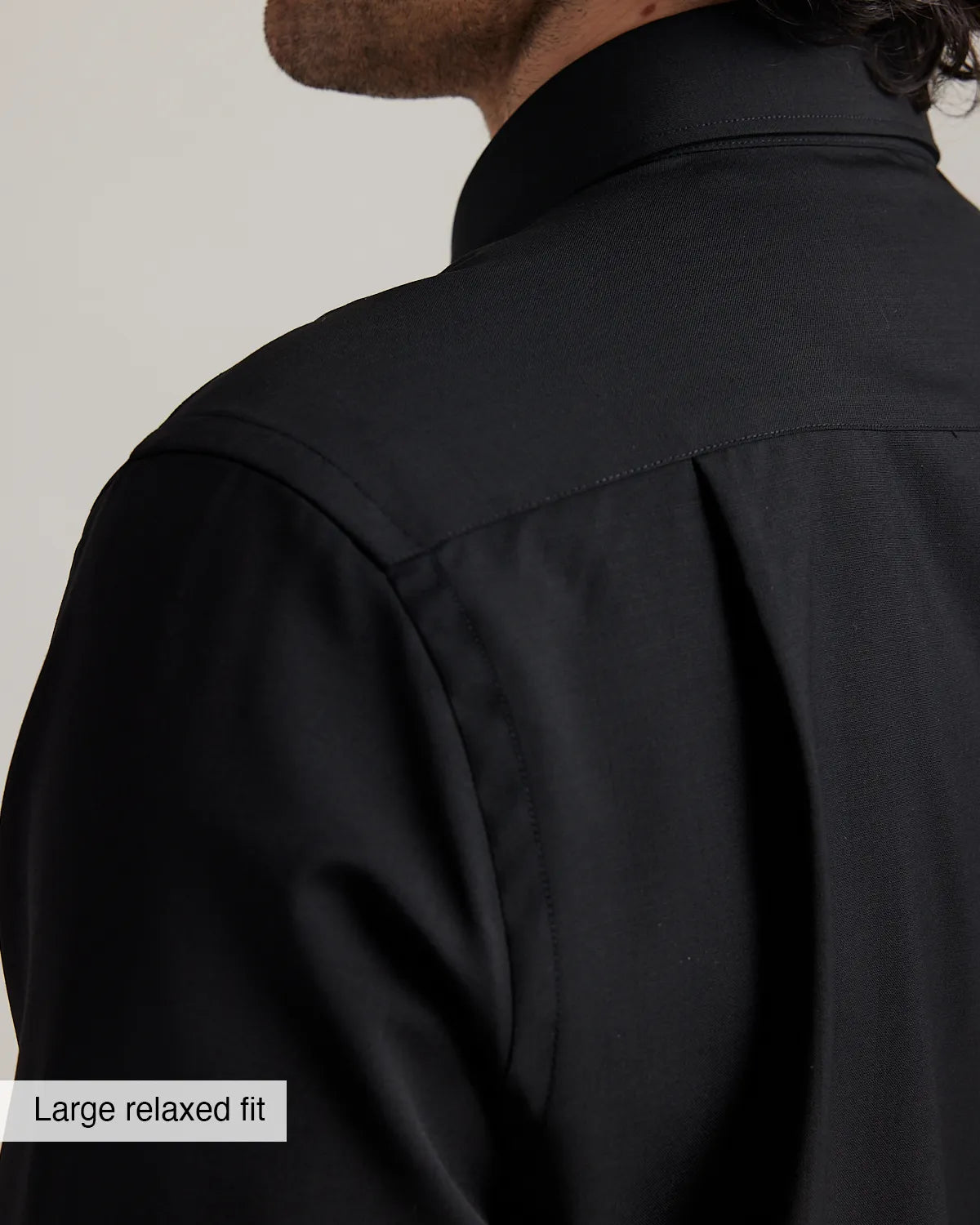 detail of the shoulder and back pleat on a black merino wool shirt with large relaxed fit label on a neutral background