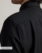 detail of the shoulder and back pleat on a black merino wool shirt with large relaxed fit label on a neutral background