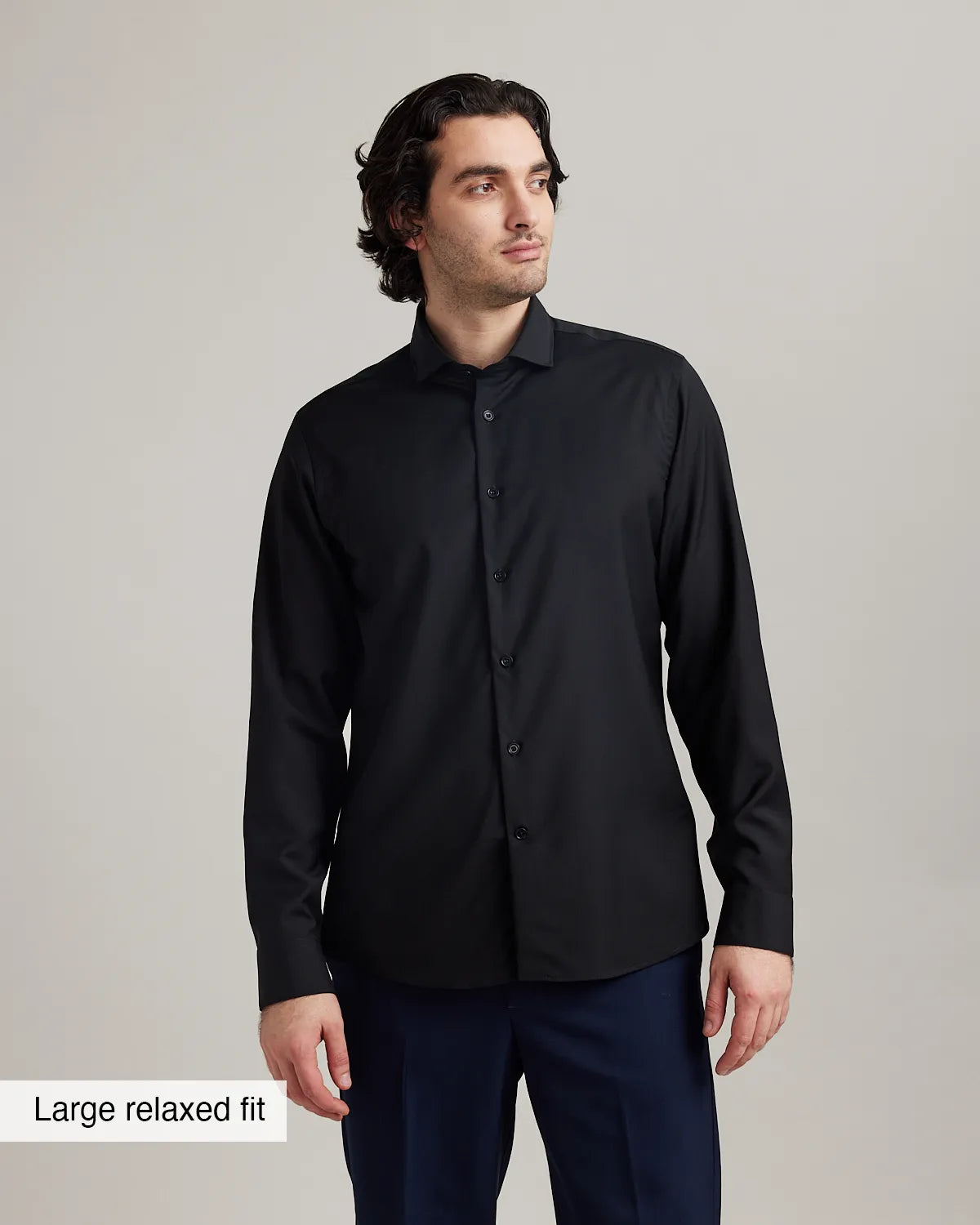 Man wearing a black merino dress shirt with a large relaxed fit label on a gray background