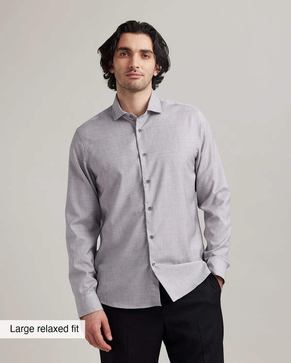 Man wearing a light gray heather merino wool buttoned shirt with a large relaxed fit label on a plain background