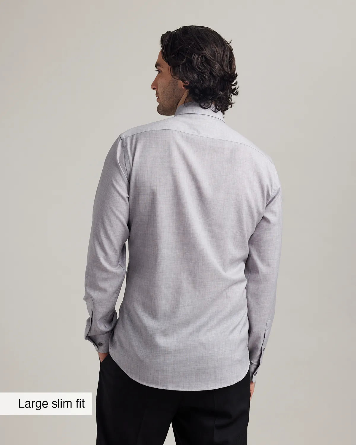Back view of a man wearing a light gray merino dress shirt with long sleeves on a plain background