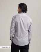 Back view of a man wearing a light gray merino dress shirt with long sleeves on a plain background