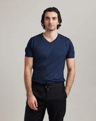 Man wearing a navy blue merino wool V-neck t-shirt and black pants on a plain background