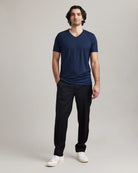 Man wearing a navy V-neck merino wool Tshirt, black pants, and white sneakers on a plain background