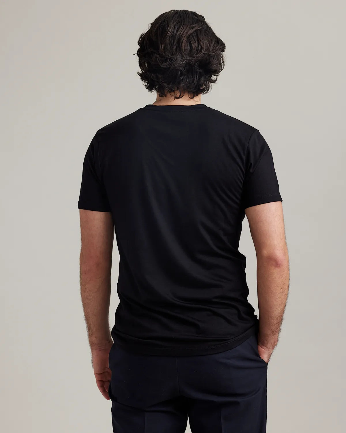 Back view of a wearing a black merino t-shirt on a plain background