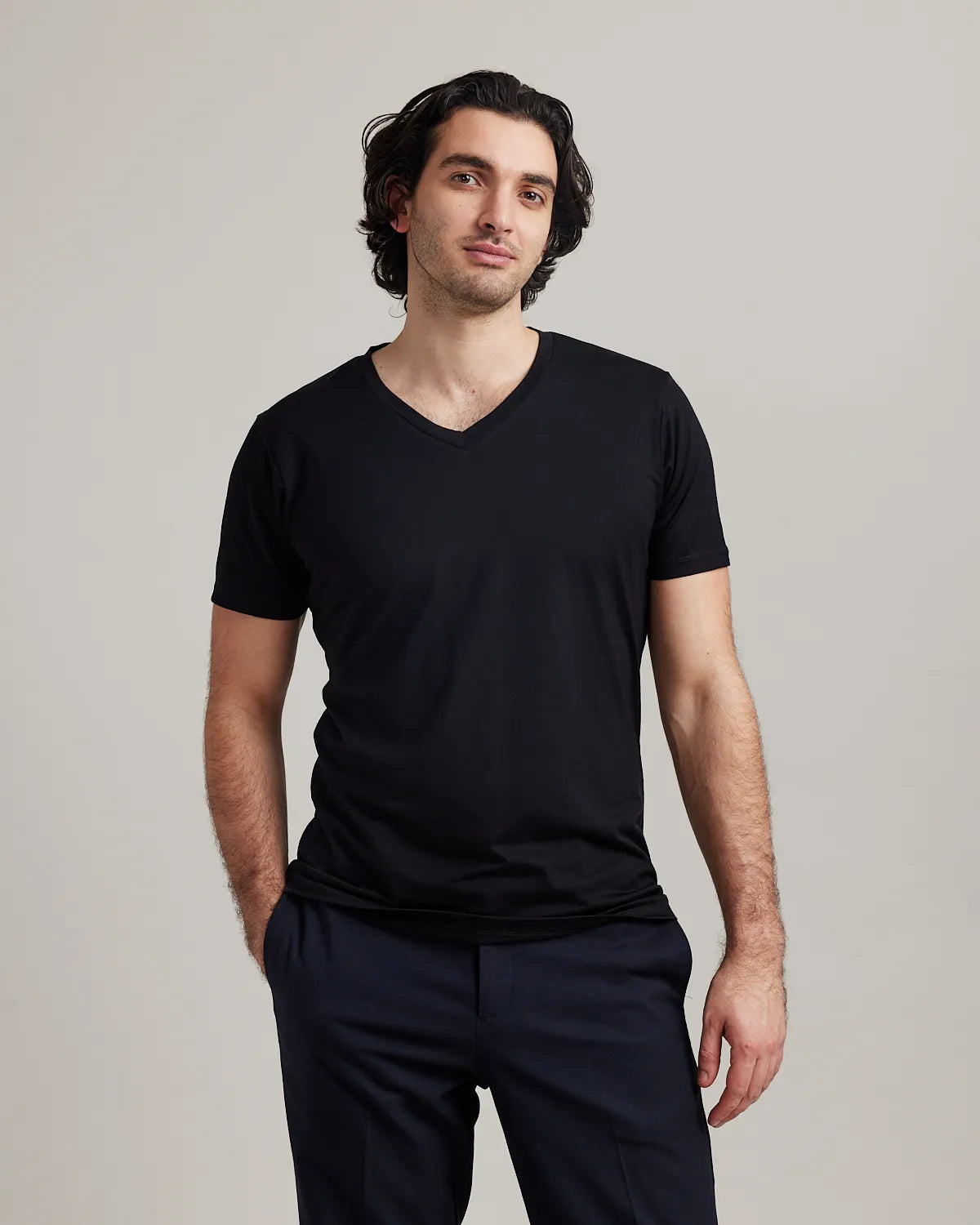 Man wearing a black merino wool V-neck t-shirt and dark pants against a plain background