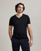 Man wearing a black merino wool V-neck t-shirt and dark pants against a plain background