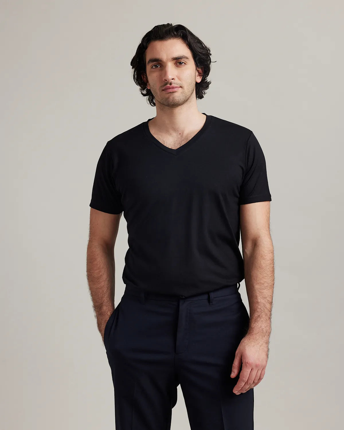 Man wearing a black V-neck merino t-shirt and dark pants against a plain background