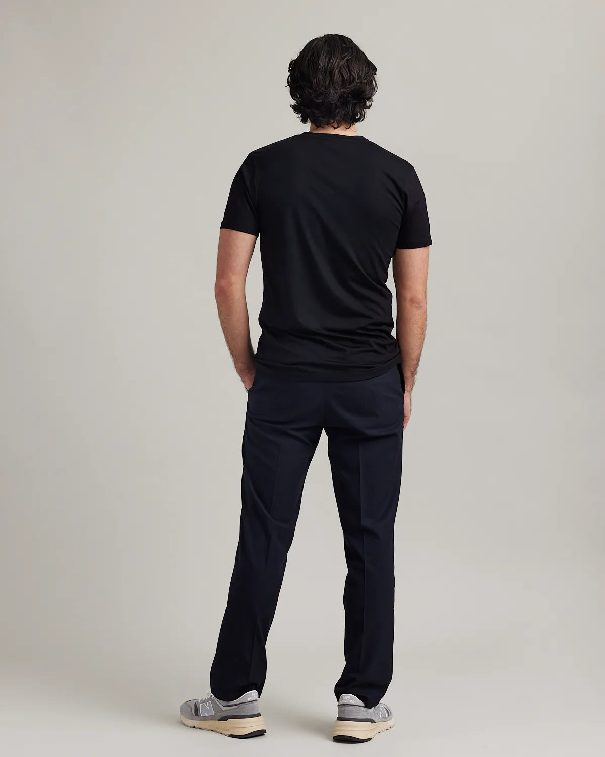 Man wearing a black merino t-shirt and navy pants on a plain background