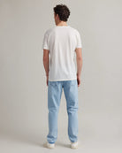 back view of a man wearing a white merino t-shirt and light blue jeans on a plain background