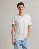 Man wearing a plain white merino wool t-shirt and light blue jeans against a neutral background