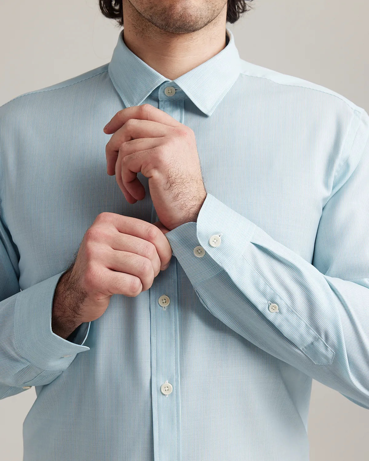 Man wearing a light blue merinowool dress shirt, adjusting the cuffs