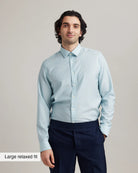 Man wearing a light blue striped merino longsleeve shirt and dark pants against a plain background