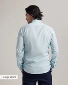 back view of a man wearing an untucked slim fit merinowool dress shirt on navy trousers with a plain background