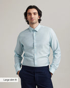 Man wearing a light blue merinowool button up shirt and dark pants against a plain background