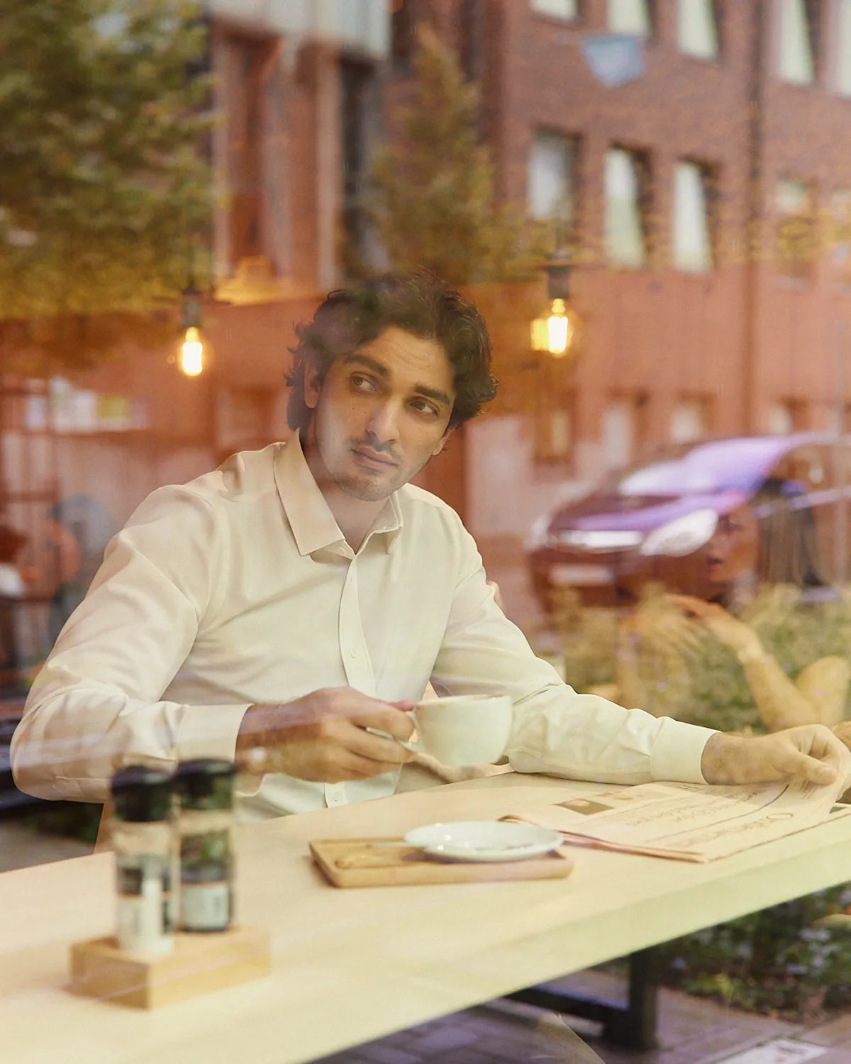 Man holding a coffee in a coffee bar wearing a white merinowool dress shirt from Wolk