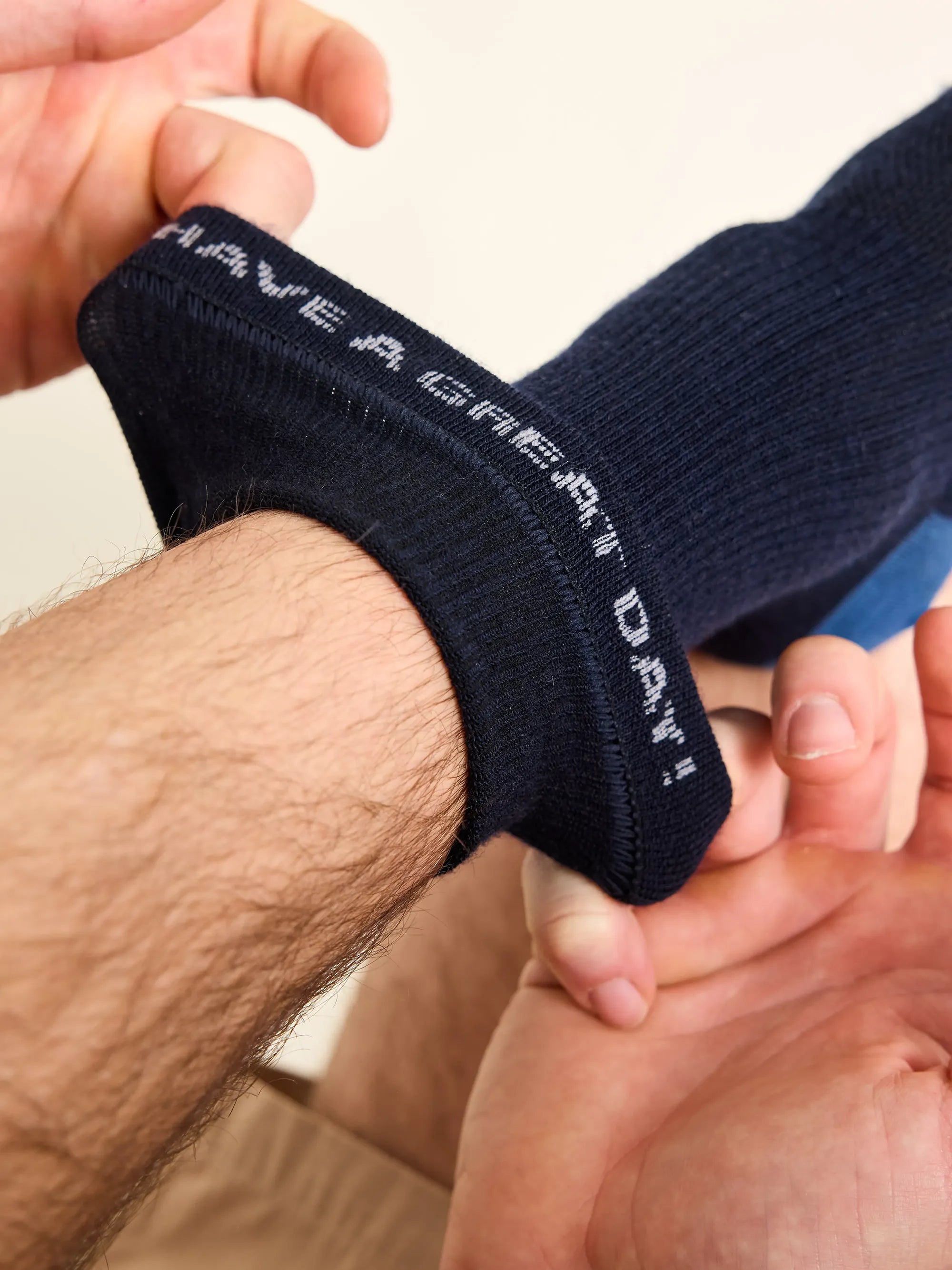 Man wears a navy merino wool sock with inside the cuff a text