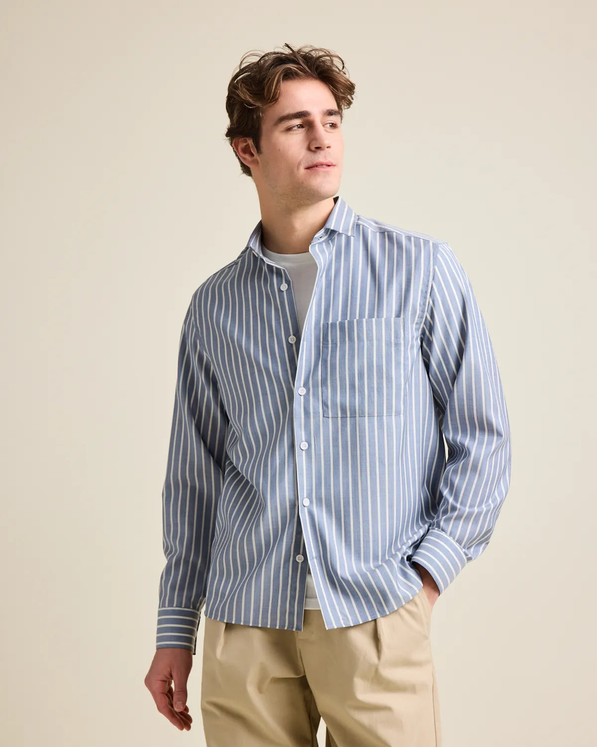 Man wearing a navy blue and white striped merino wool button up shirt against a beige background