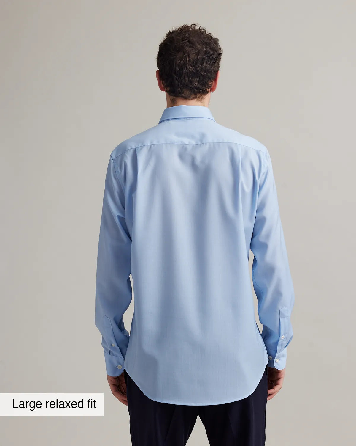 Back view of a man wearing a light blue merinowool shirt with text 'Large relaxed fit' on a gray background