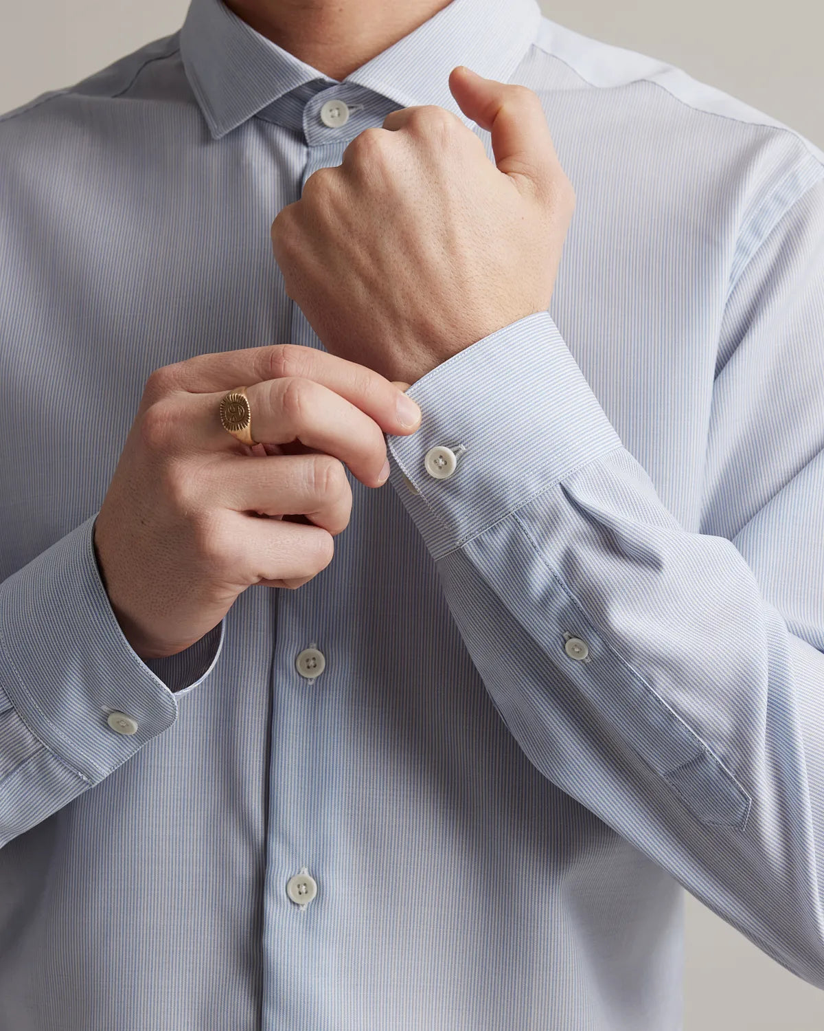 Person adjusting the cuff of a light blue merino dress shirt with a neutral background