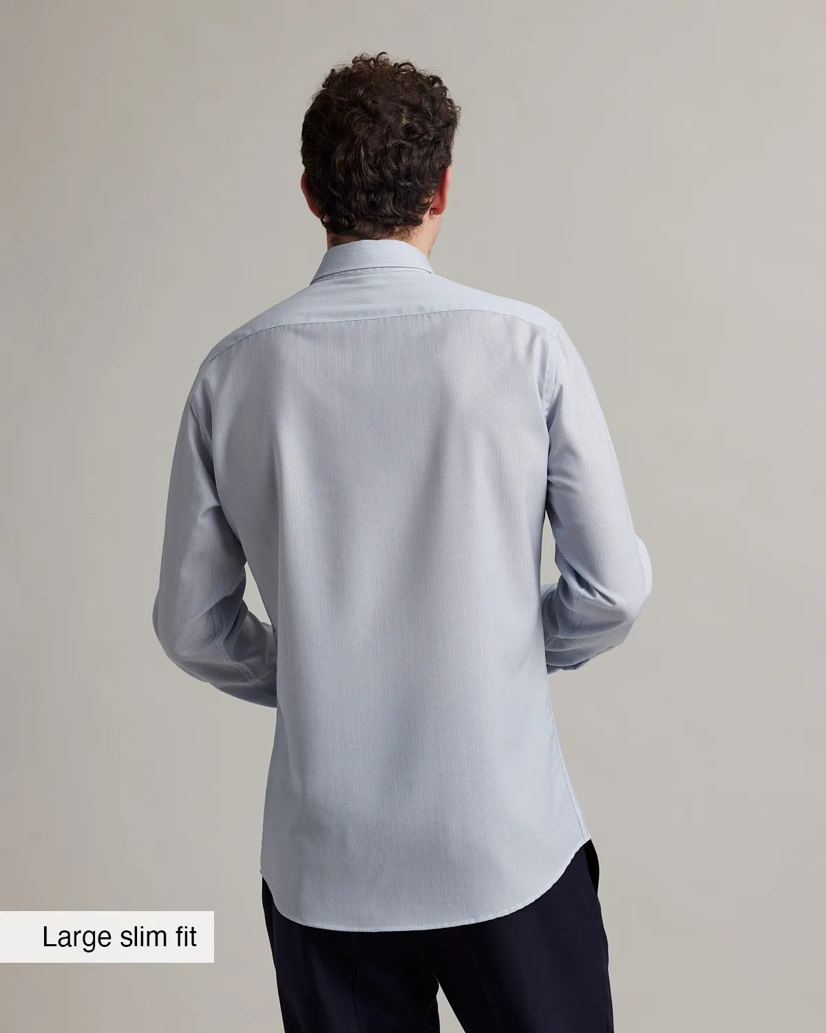 Back view of a man wearing a light gray merino wool dress shirt on a plain background