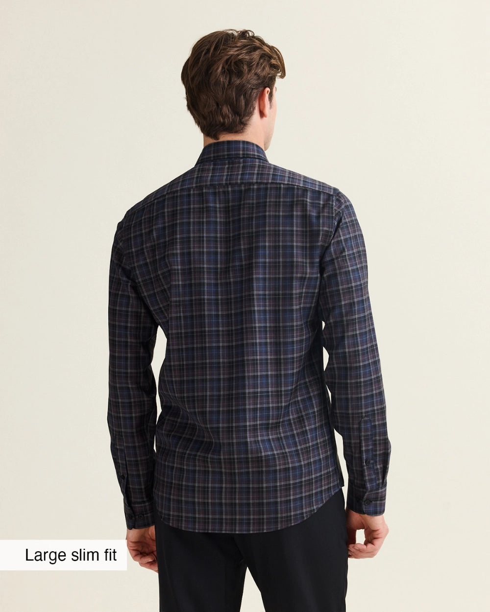 A man viewed from the back wearing a dark navy plaid Wolk merino shirt with black trousers, set against a plain light beige background. A text label in the bottom-left corner reads 'Large slim fit'.