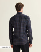 A man viewed from the back wearing a dark navy plaid Wolk merino shirt with black trousers, set against a plain light beige background. A text label in the bottom-left corner reads 'Large slim fit'.