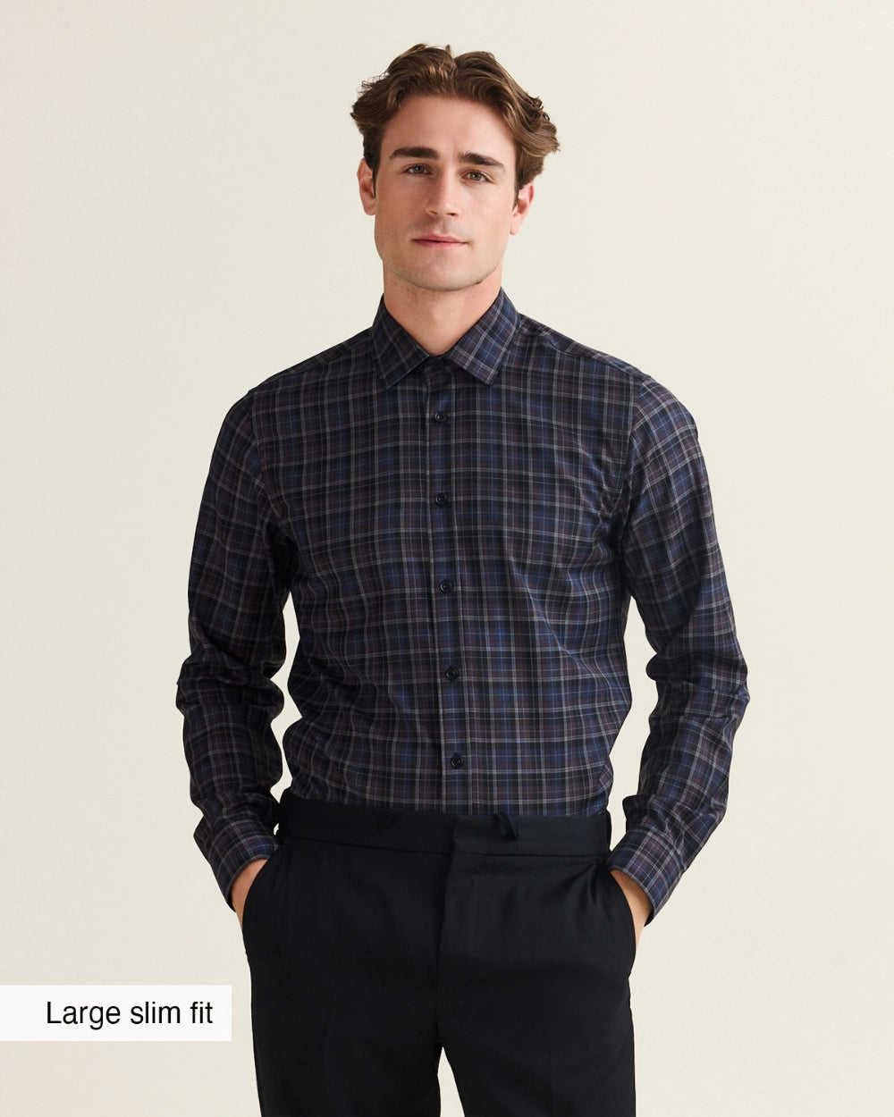 A man wearing a dark navy and black plaid long-sleeve dress Wolk merino shirt with a slim fit, paired with black trousers, against a light beige background. A text overlay in the bottom-left corner reads 'Large slim fit'.