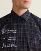 Close-up of a man wearing a dark navy and black, purple plaid merino shirt, with white text overlays highlighting features like 'No Odour, Stay Fresh', 'Wrinkle Resistant', and 'Thermo Regulating'.