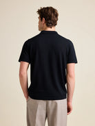 A male model in the studio wears a black merino wool polo shirt from the European brand Wolk.
