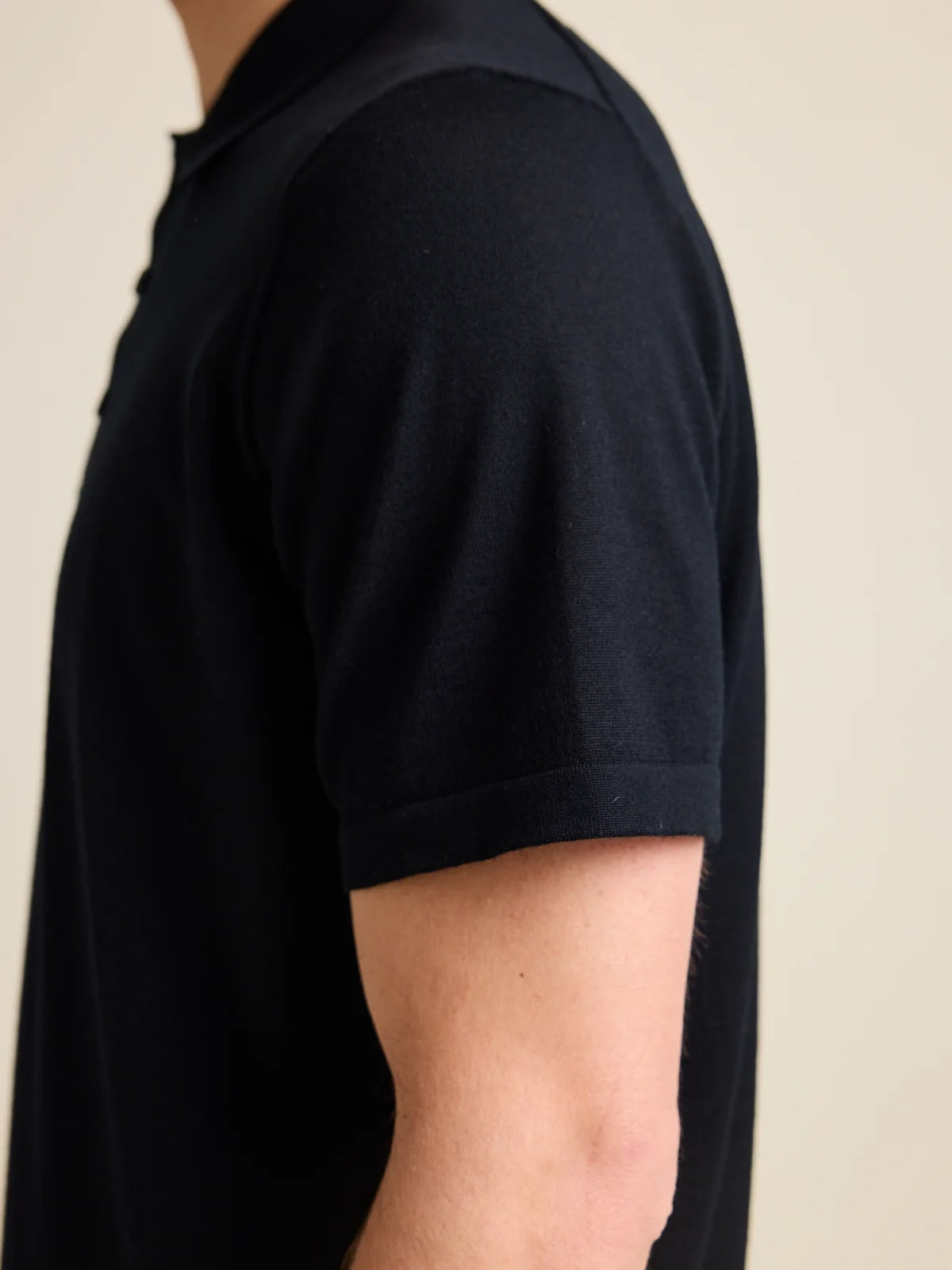 Close-up of the short sleeve on a men's black merino wool polo shirt by Wolk, showcasing the luxrious cashwool knit.