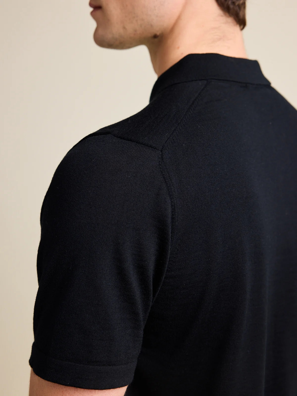 Shoulder detail of a men's black merino wool Polo shirt from Wolk, emphasizing the luxurious Cashwool knit.