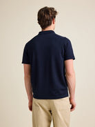 Back view of man wearing a short sleeve merino wool polo in dark navy blue color.