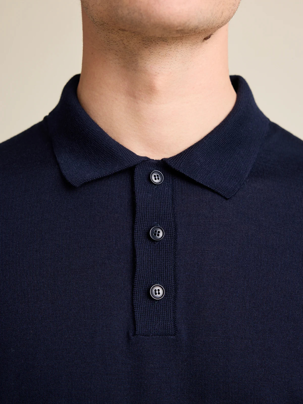 detail of knitted collar of a navy blue knitted merino wool polo shirt, with 3 corozo buttons in navy color.