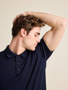 Man smells his armpits  to show that his merino wool polo in navy color and short sleeves from Wolk doesn't smell and doesn't take up odours.