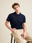 Caucasian man with brown hair sits on high chair wearing a high quality merino wool polo shirtmade with Zegna cashwool in dark navy color.
