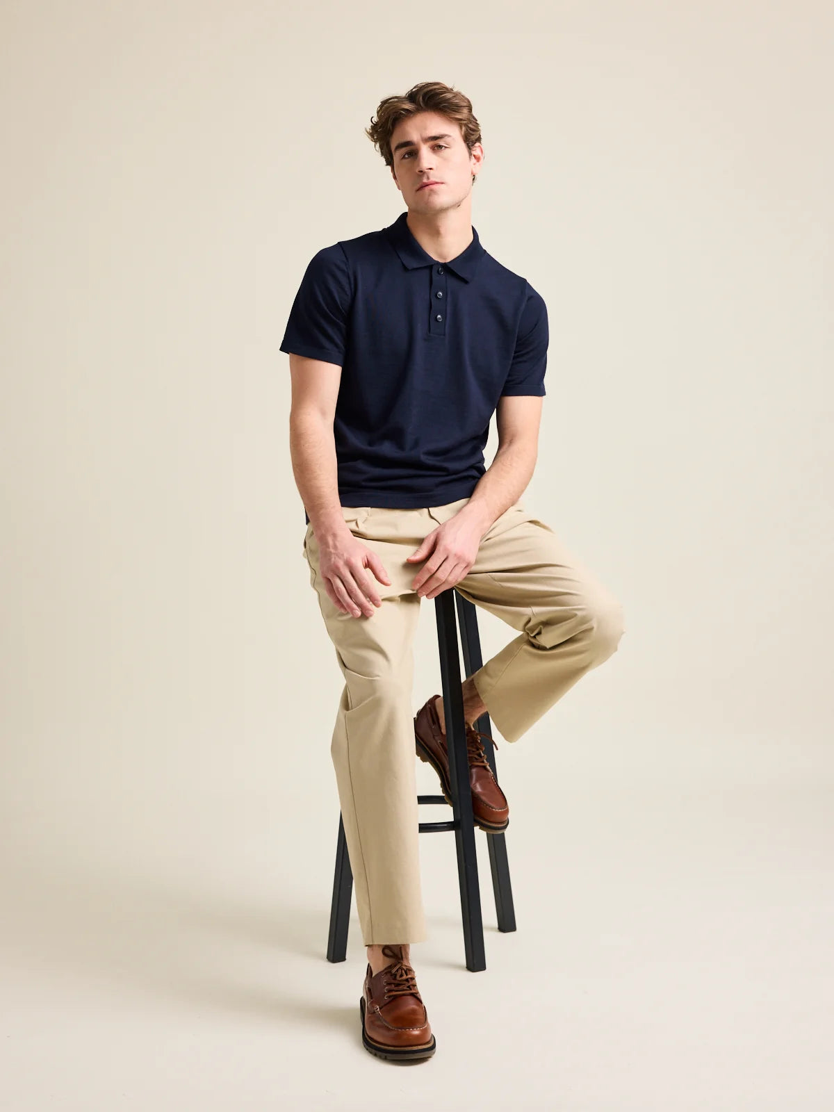 man sits on high chair wearing a short sleeve merino wool polo in dark navy color. Made in Europe (Portugal)