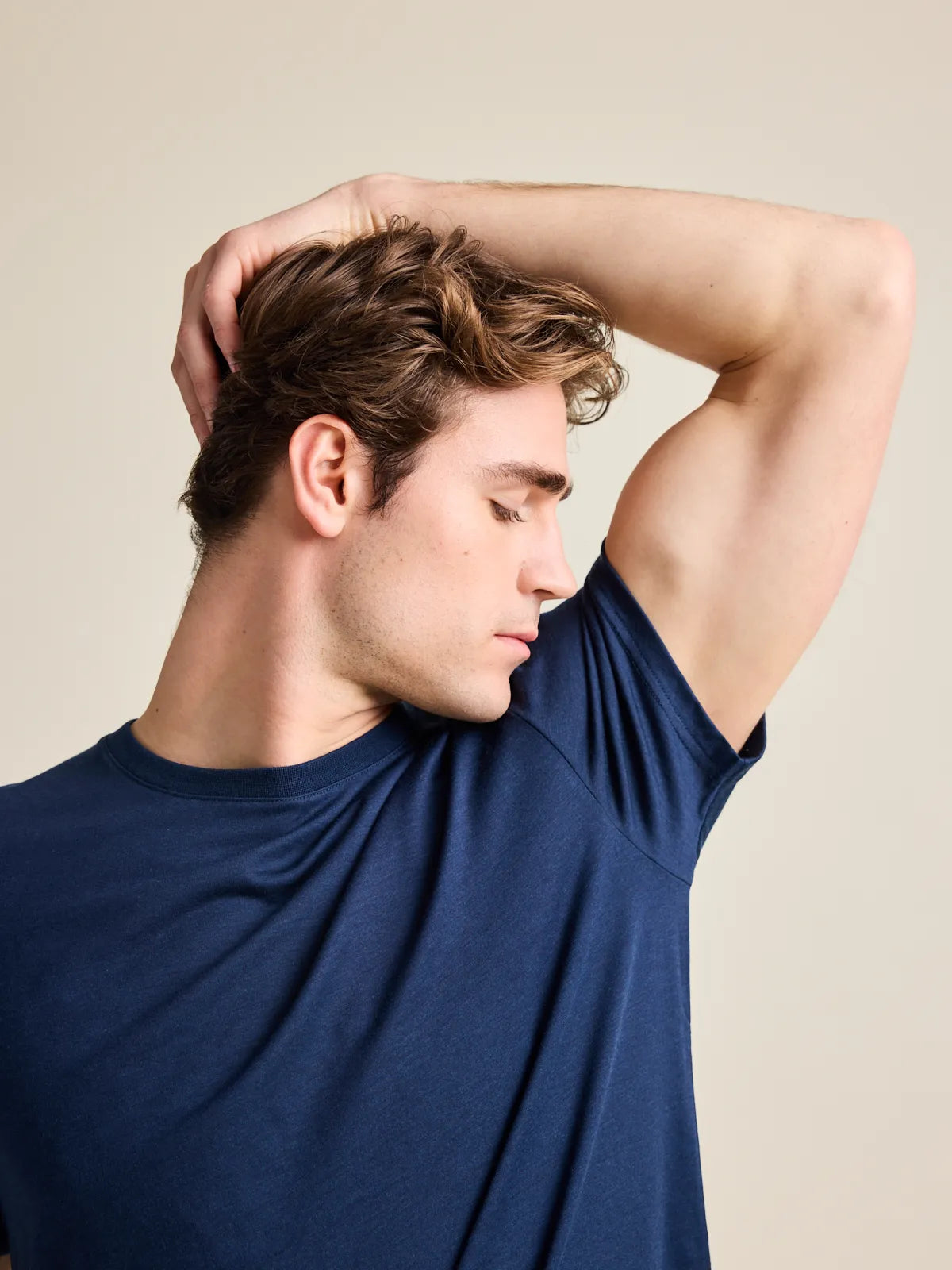 Man smells armpit and wears a navy blue merino wool T-shirts that is free of odours.