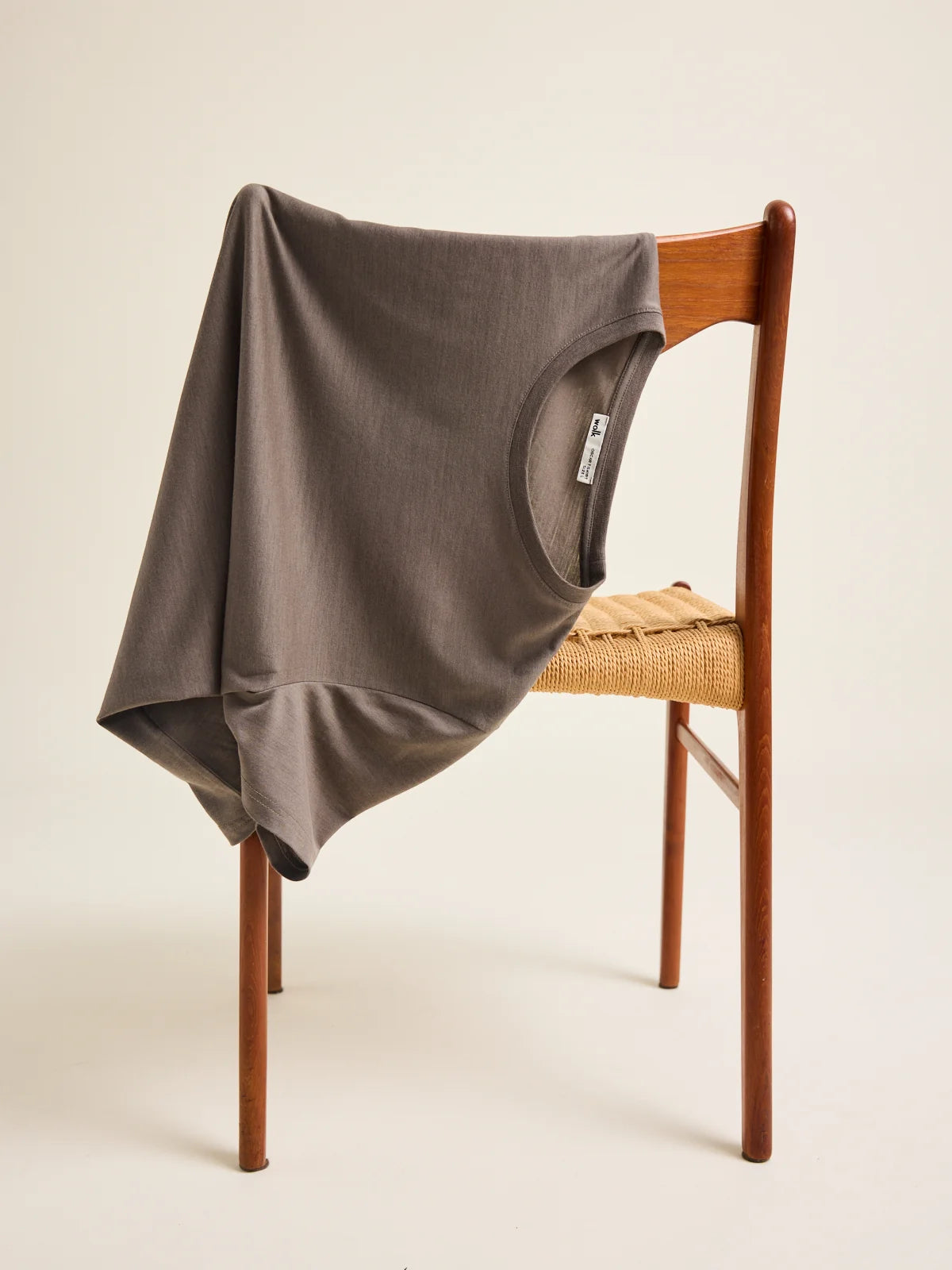 A chocolate brown merino wool t-shirt from the brand Wolk is draped over a vintage chair in a studio setting.