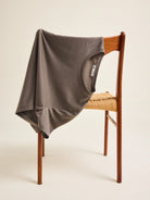 A chocolate brown merino wool t-shirt from the brand Wolk is draped over a vintage chair in a studio setting.