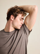 Male man in a studio setting sniffing the armpit of a chocolate brown wool T-shirt from the Wolk brand.