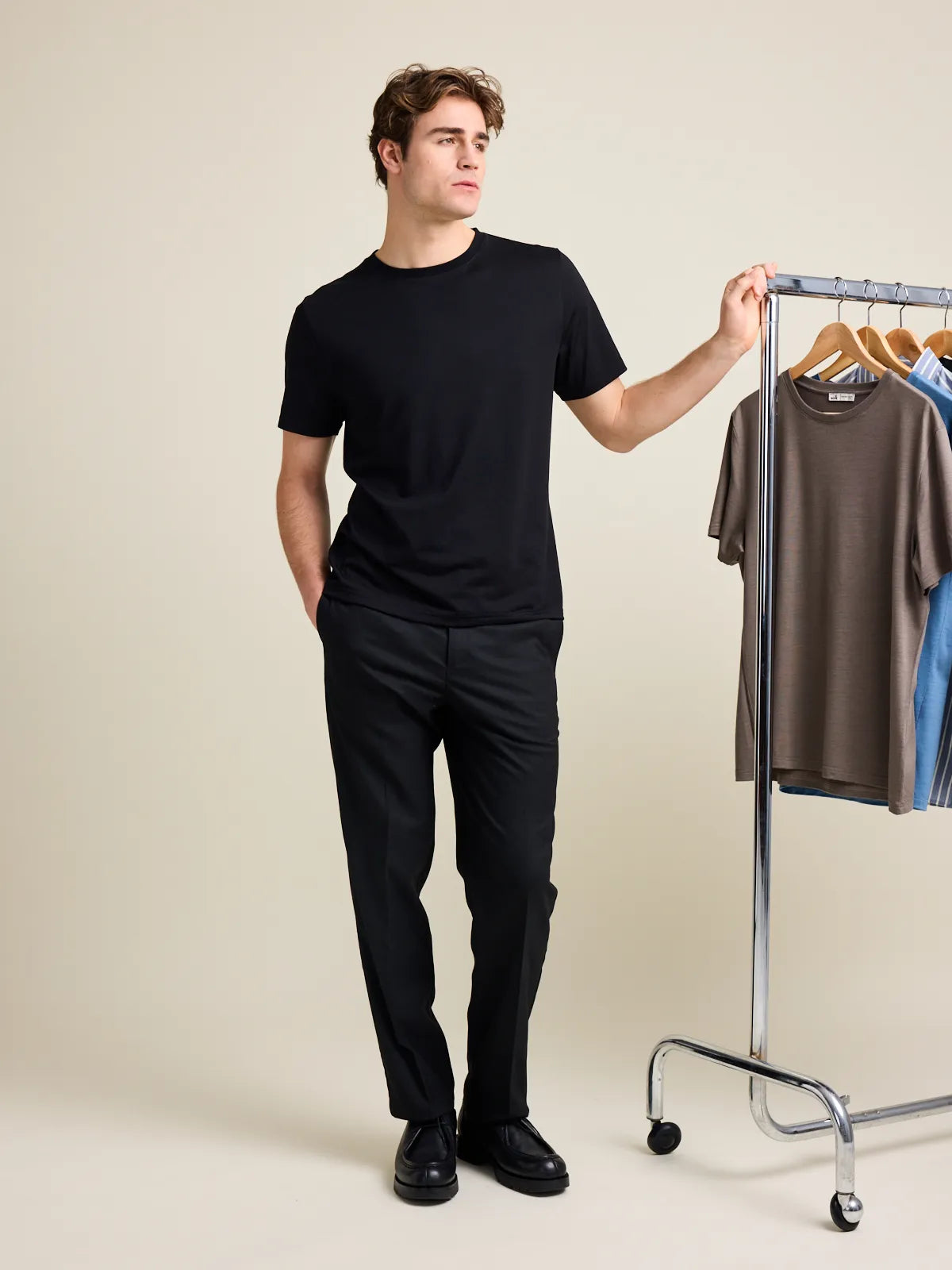 Man wears stylish merino T-shirt in black with round neck and short sleeves on black trousers.