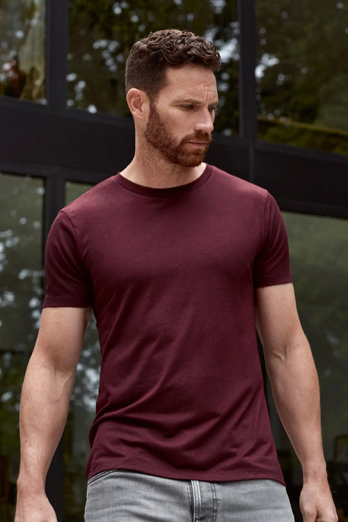Un homme porte un T-shirt en laine mérinos bordeaux à col rond et à manches courtes de Wolk.